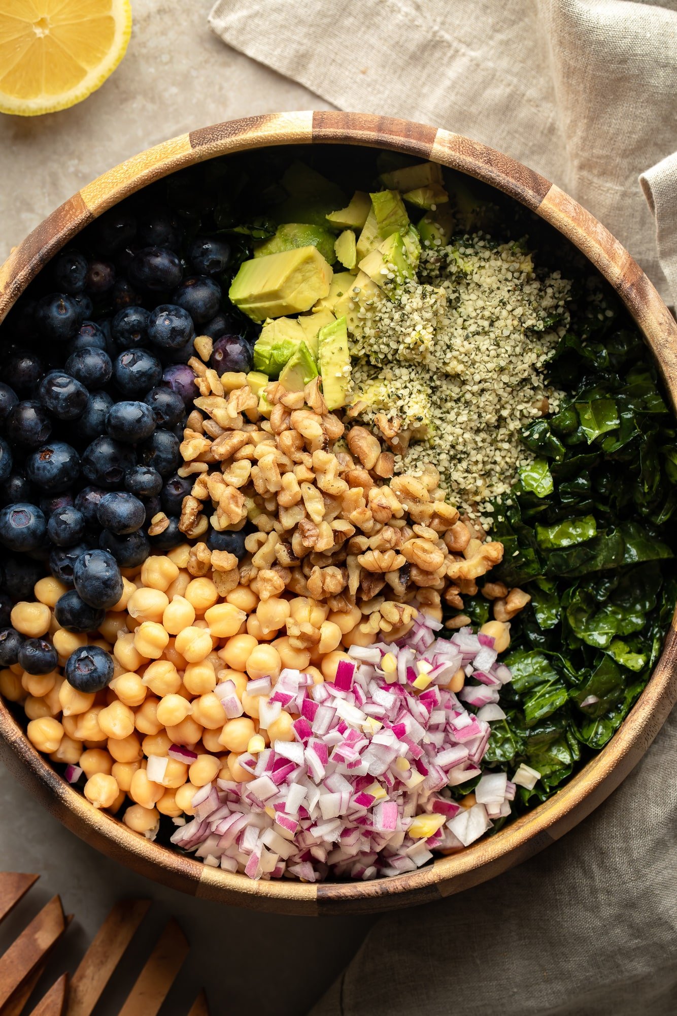 Uma salada de couve coberta com sementes, nozes, feijões, vegetais e frutas em uma grande tigela de salada.