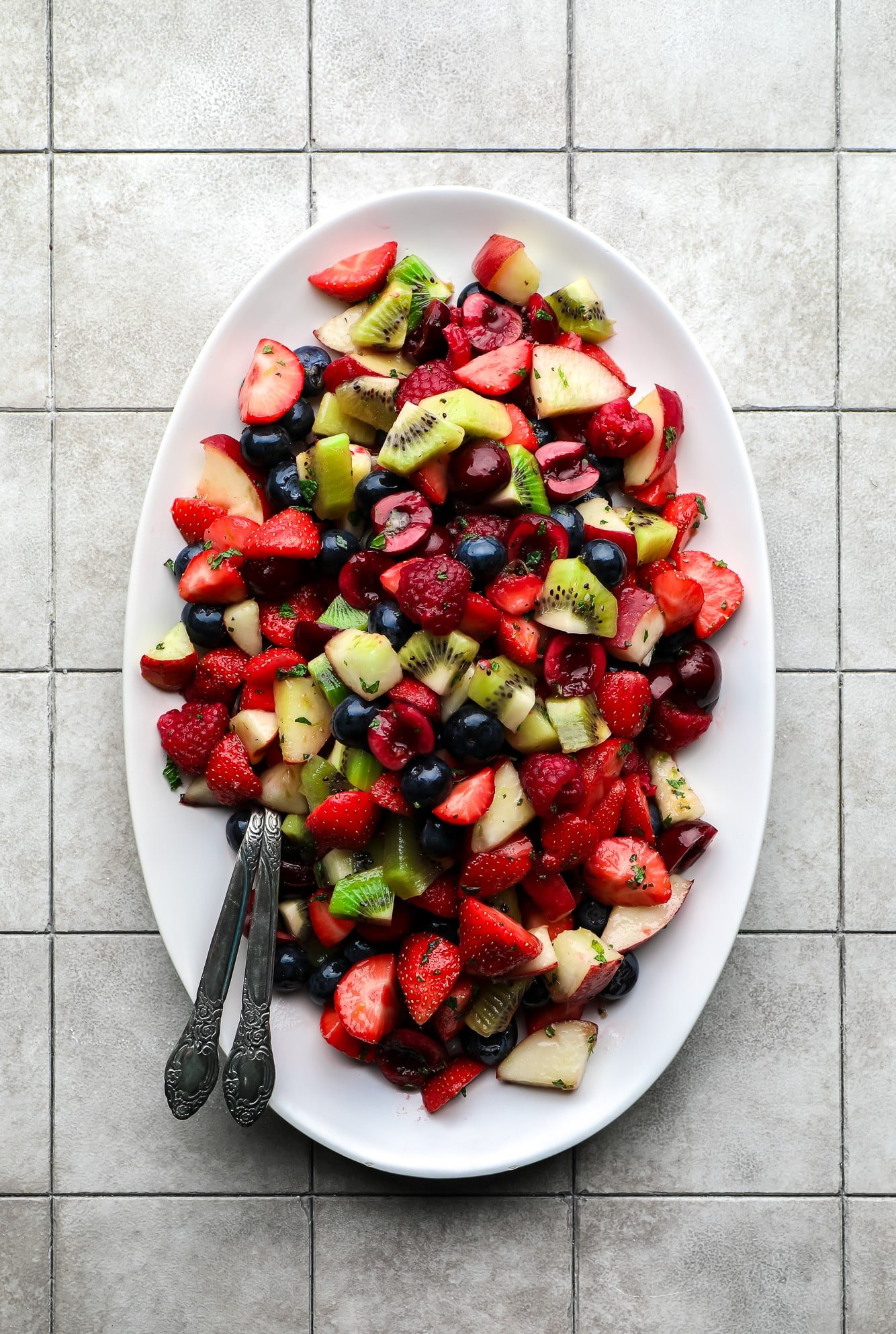 Salada de frutas em um prato branco com duas colheres.