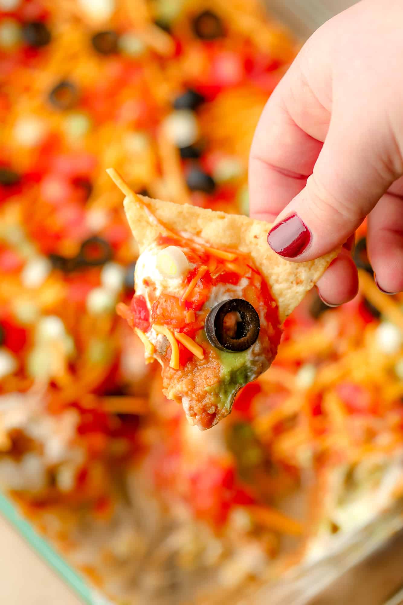 Mão da mulher segurando um chip de tortilla que foi mergulhado em mergulho vegano de 7 camadas.